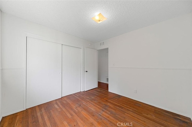 unfurnished bedroom with a closet, visible vents, dark wood finished floors, and a textured ceiling