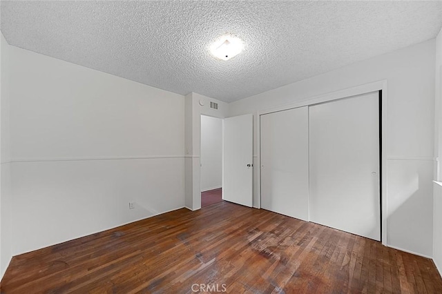 unfurnished bedroom with dark wood-style floors, a closet, a textured ceiling, and visible vents