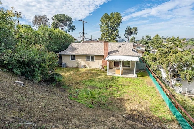 back of house with fence, roof with shingles, a lawn, stucco siding, and a chimney