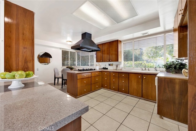 kitchen with a sink, light countertops, island exhaust hood, and brown cabinets