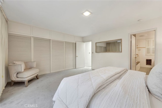 bedroom with a closet, ensuite bath, visible vents, and light colored carpet