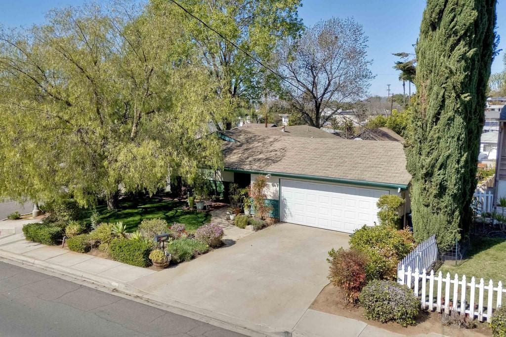 view of front of home with driveway, an attached garage, fence, and a shingled roof