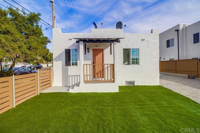 rear view of property featuring a lawn, fence, and stucco siding