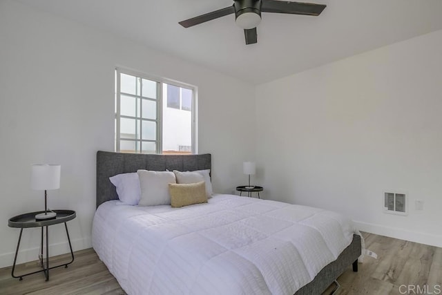 bedroom with ceiling fan, light wood finished floors, visible vents, and baseboards