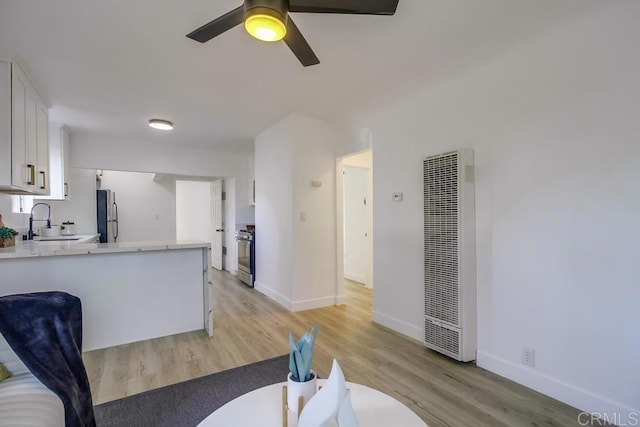 kitchen with a heating unit, white cabinets, stainless steel appliances, light countertops, and a sink