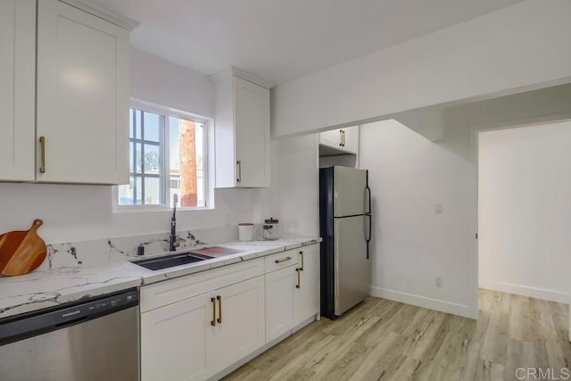 kitchen with light stone counters, a sink, light wood-style floors, white cabinets, and appliances with stainless steel finishes