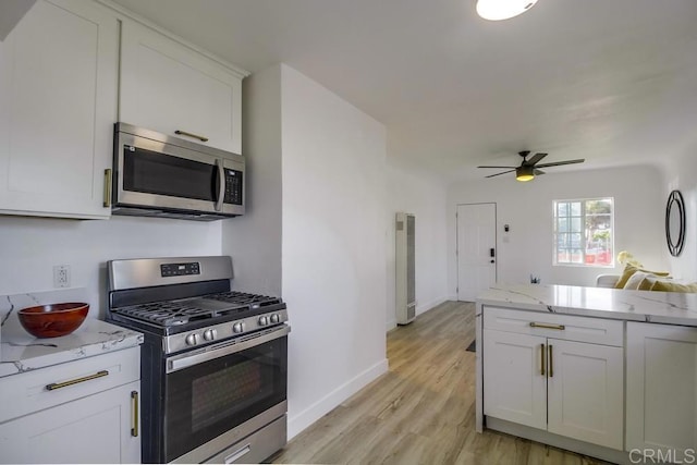 kitchen with light stone counters, light wood finished floors, stainless steel appliances, open floor plan, and white cabinets