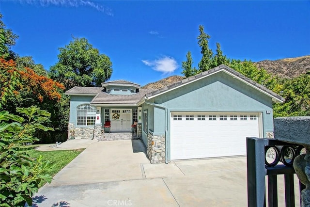 view of front of property featuring an attached garage, a tile roof, stone siding, concrete driveway, and stucco siding