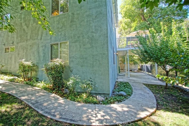 view of side of home with a patio area, stairs, fence, and stucco siding