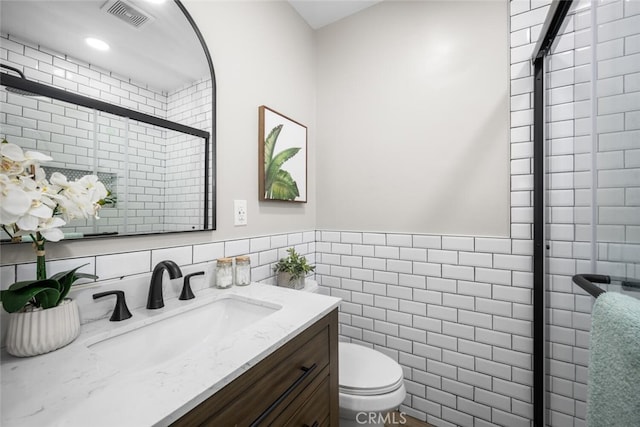 bathroom with visible vents, toilet, vanity, a shower stall, and tile walls