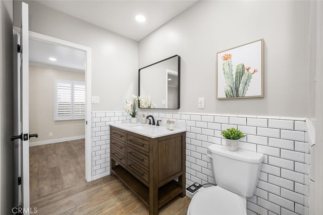 bathroom with tile walls, toilet, wainscoting, vanity, and wood finished floors