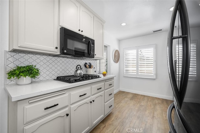 kitchen with white cabinets, black appliances, light countertops, and backsplash