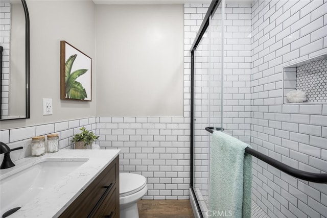 bathroom with toilet, vanity, tile walls, wainscoting, and a stall shower