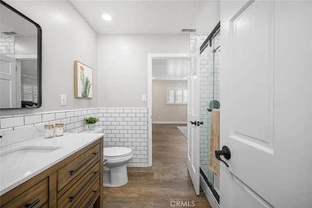 bathroom featuring visible vents, toilet, wood finished floors, vanity, and tile walls