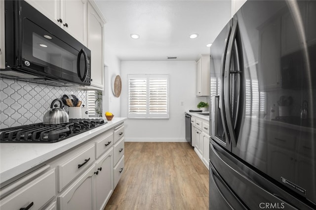 kitchen featuring tasteful backsplash, light countertops, light wood-style flooring, white cabinets, and black appliances