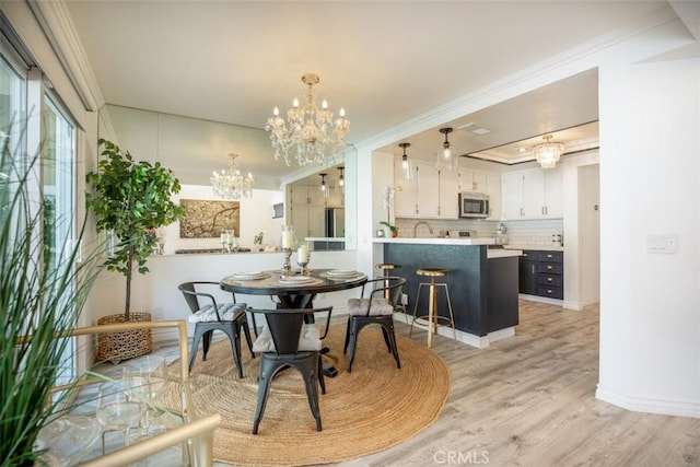 dining area with a chandelier, baseboards, light wood-style floors, ornamental molding, and a tray ceiling