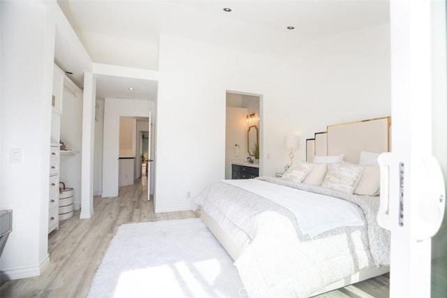 bedroom with light wood-type flooring, baseboards, and connected bathroom