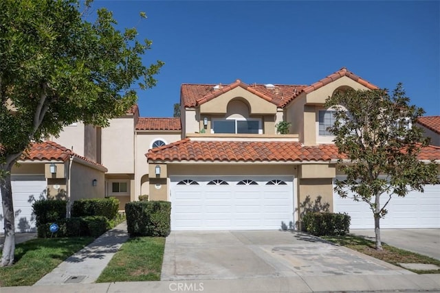 mediterranean / spanish-style home featuring concrete driveway, a tile roof, an attached garage, and stucco siding