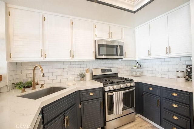 kitchen with white cabinetry, dark cabinetry, appliances with stainless steel finishes, and a sink