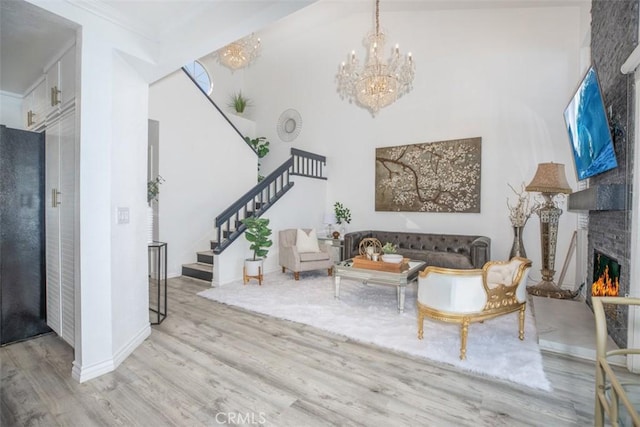 living room featuring light wood finished floors, an inviting chandelier, ornamental molding, a brick fireplace, and stairs