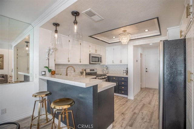 kitchen with stainless steel appliances, visible vents, white cabinetry, light countertops, and a tray ceiling