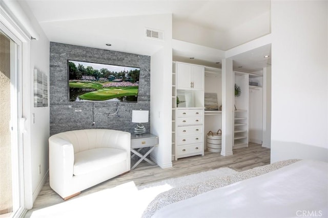 bedroom featuring light wood finished floors, baseboards, visible vents, lofted ceiling, and an accent wall