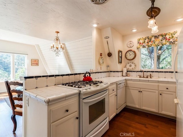 kitchen with a peninsula, white appliances, tile countertops, and decorative light fixtures