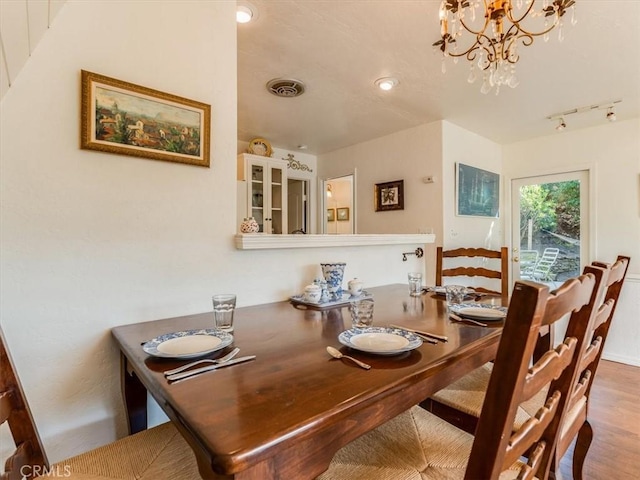 dining area with an inviting chandelier, track lighting, visible vents, and wood finished floors