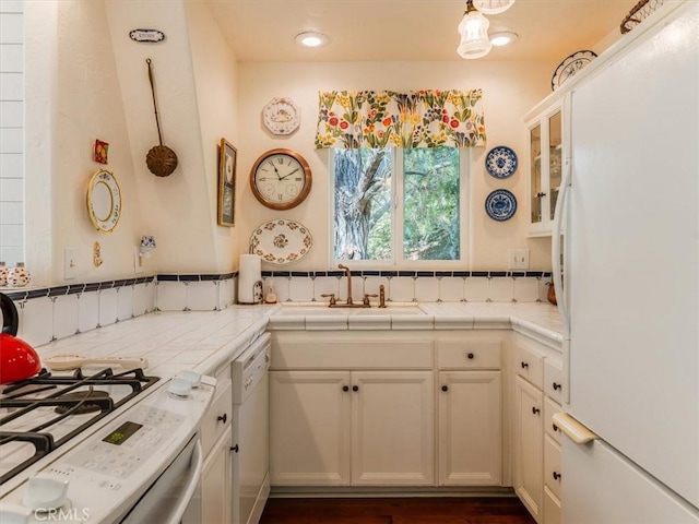 kitchen with tile countertops, hanging light fixtures, white cabinets, a sink, and white appliances