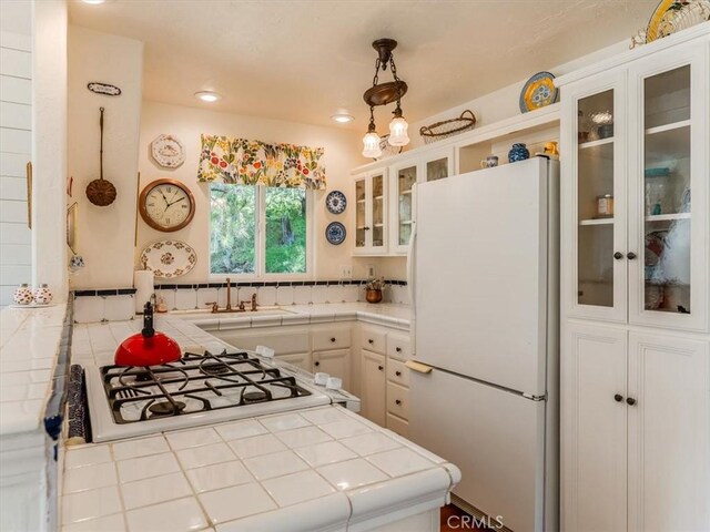 kitchen with tile counters, white cabinets, glass insert cabinets, freestanding refrigerator, and a sink