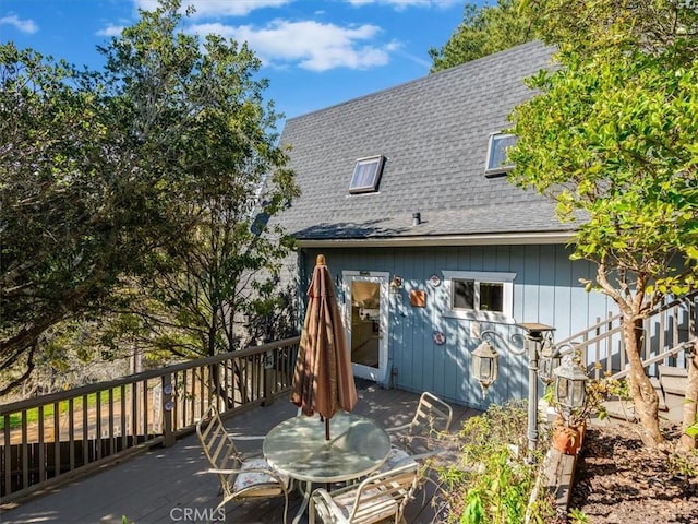 rear view of house with outdoor dining area, roof with shingles, and a wooden deck