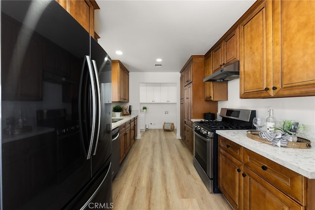 kitchen with appliances with stainless steel finishes, brown cabinets, light stone countertops, light wood-type flooring, and under cabinet range hood