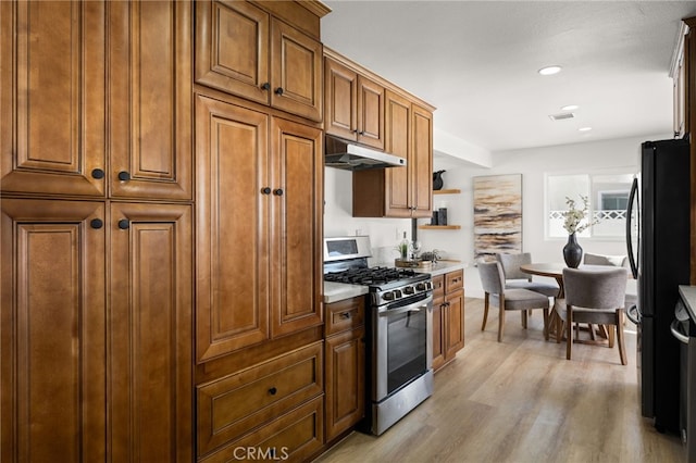 kitchen featuring gas range, freestanding refrigerator, light countertops, under cabinet range hood, and open shelves