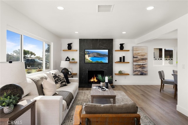 living area with recessed lighting, wood finished floors, visible vents, and a high end fireplace