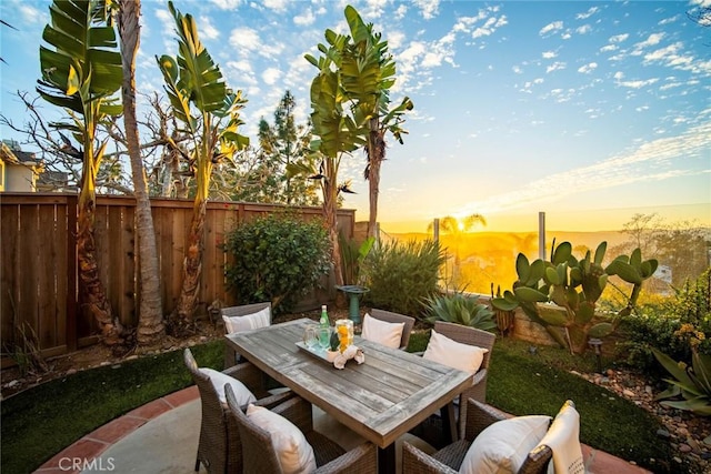 patio terrace at dusk with outdoor dining space and a fenced backyard