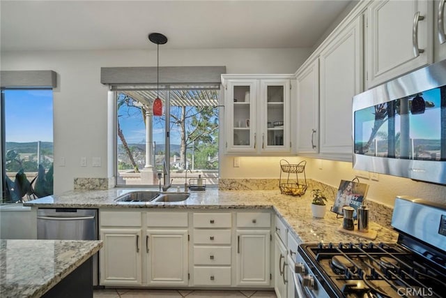 kitchen featuring glass insert cabinets, appliances with stainless steel finishes, decorative light fixtures, white cabinetry, and a sink