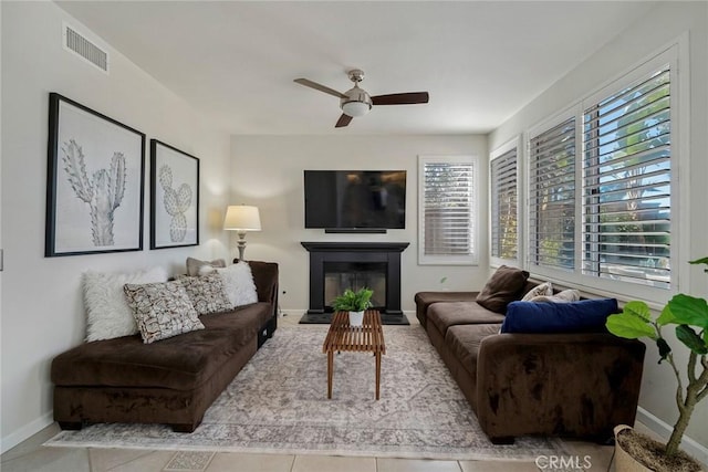 living area featuring light tile patterned floors, visible vents, baseboards, a fireplace with flush hearth, and ceiling fan