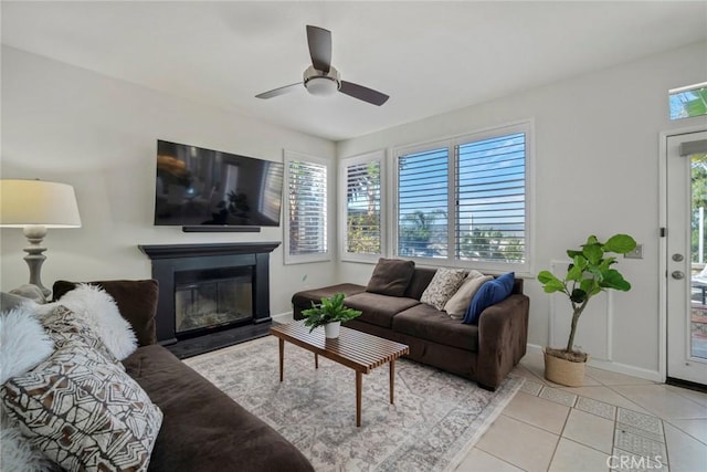 living area featuring baseboards, a glass covered fireplace, a ceiling fan, and light tile patterned flooring