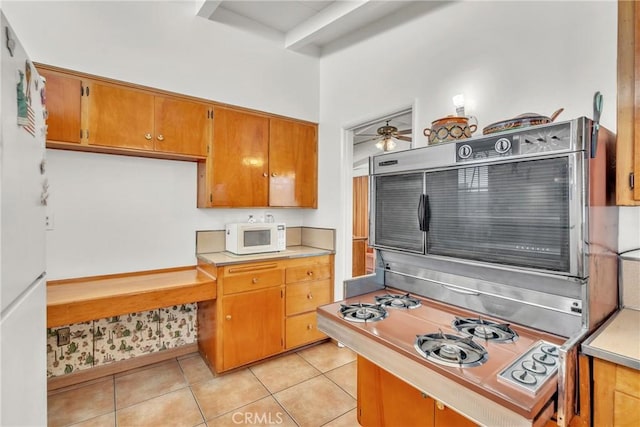 kitchen with brown cabinetry, white appliances, light countertops, and light tile patterned flooring