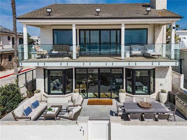 rear view of property with a balcony, outdoor lounge area, fence, a chimney, and a patio area