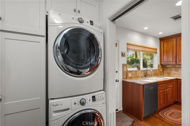 laundry area with recessed lighting, wood finished floors, a sink, visible vents, and stacked washer / drying machine