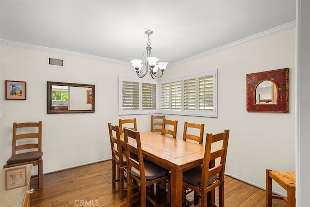 dining room with a notable chandelier, wood finished floors, visible vents, and crown molding