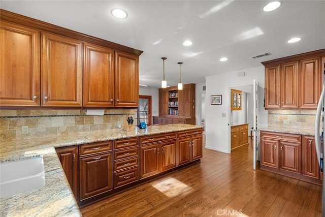 kitchen featuring decorative light fixtures, light stone countertops, visible vents, brown cabinetry, and wood finished floors