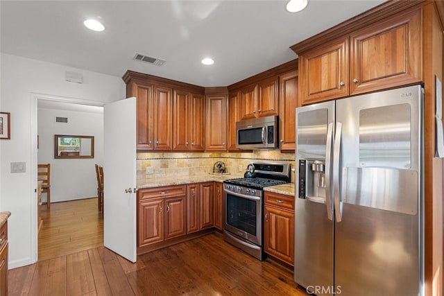 kitchen featuring dark wood-style flooring, brown cabinets, stainless steel appliances, visible vents, and light stone countertops