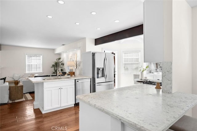 kitchen with appliances with stainless steel finishes, open floor plan, light stone countertops, white cabinetry, and a sink