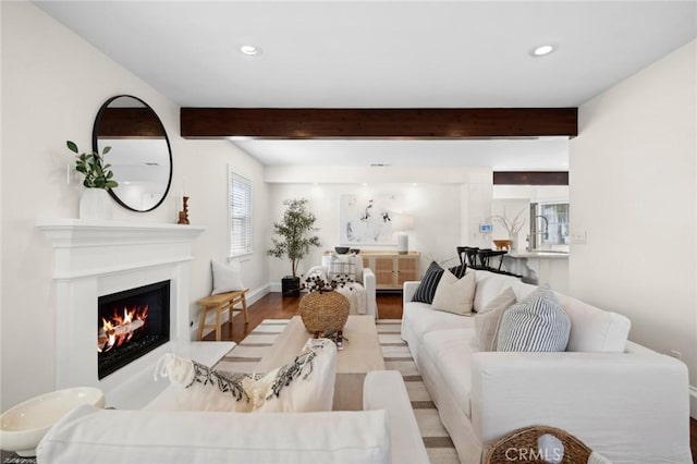 living room with recessed lighting, wood finished floors, beamed ceiling, a lit fireplace, and baseboards