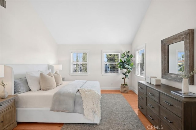 bedroom with high vaulted ceiling, light wood-type flooring, visible vents, and baseboards