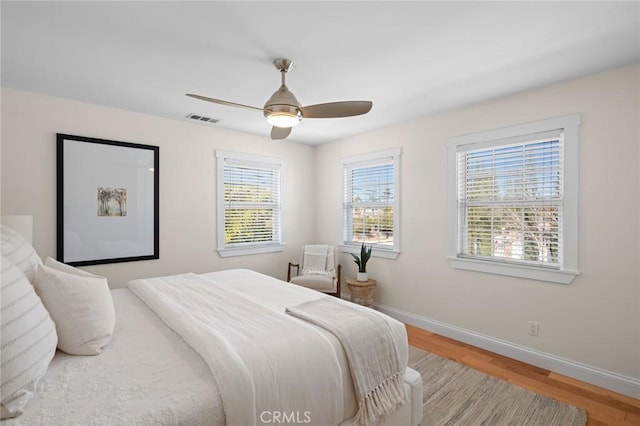 bedroom featuring a ceiling fan, wood finished floors, visible vents, and baseboards