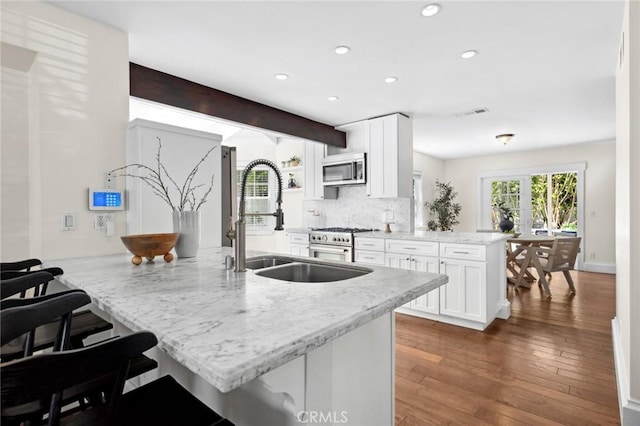 kitchen with a peninsula, a sink, white cabinets, appliances with stainless steel finishes, and light stone countertops