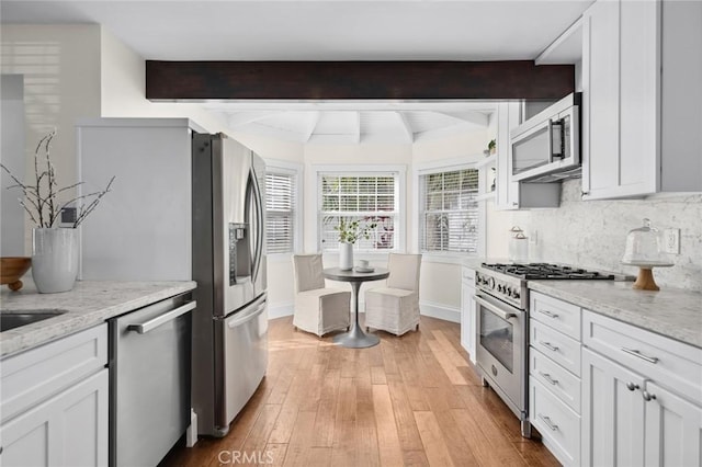 kitchen featuring white cabinets, decorative backsplash, light stone countertops, stainless steel appliances, and light wood-style floors